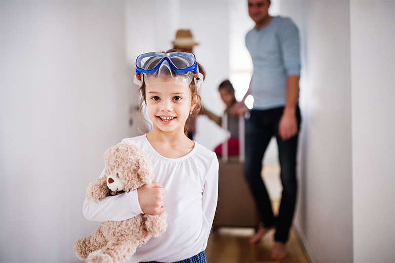 Girl holding a teddy bear as her parents carry suitcases behind her